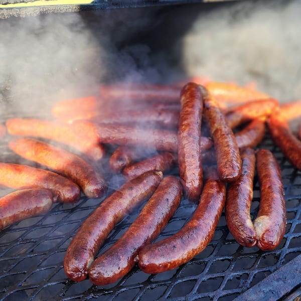 Sizzling sausages cooking on a smoky grill, with flames visible beneath the grate.