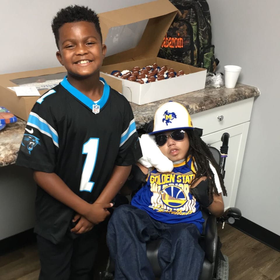 Two young boys, one in a Panthers jersey and the other in a Golden State Warriors shirt, smiling.