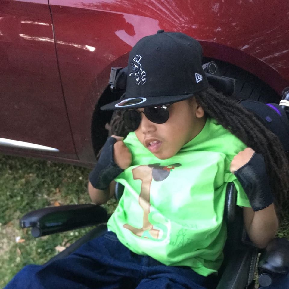 A young person in a wheelchair, wearing a black cap, sunglasses, and a lime green shirt.